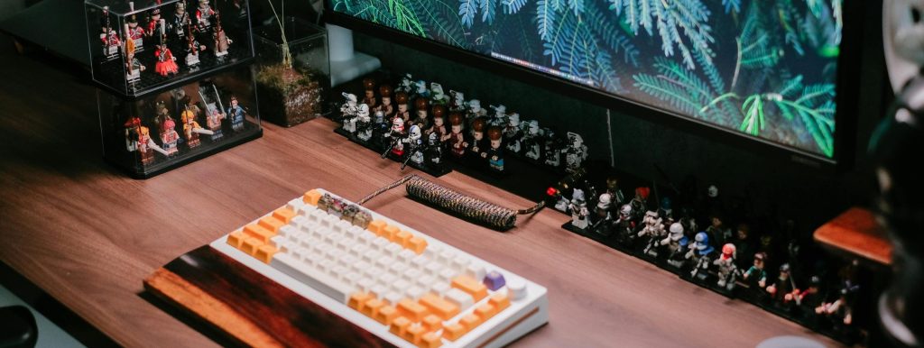 Modern desk setup featuring a custom keyboard, monitor, and collectible figurines for a tech-savvy workspace.